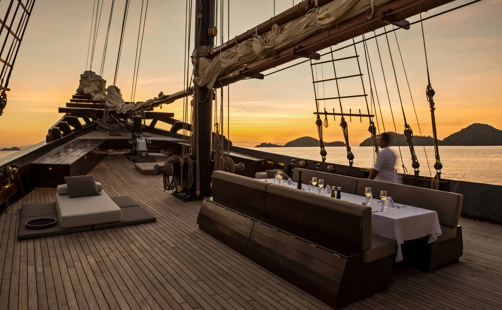 Two-masted Amandira phinisi under full white sail at golden hour near Komodo