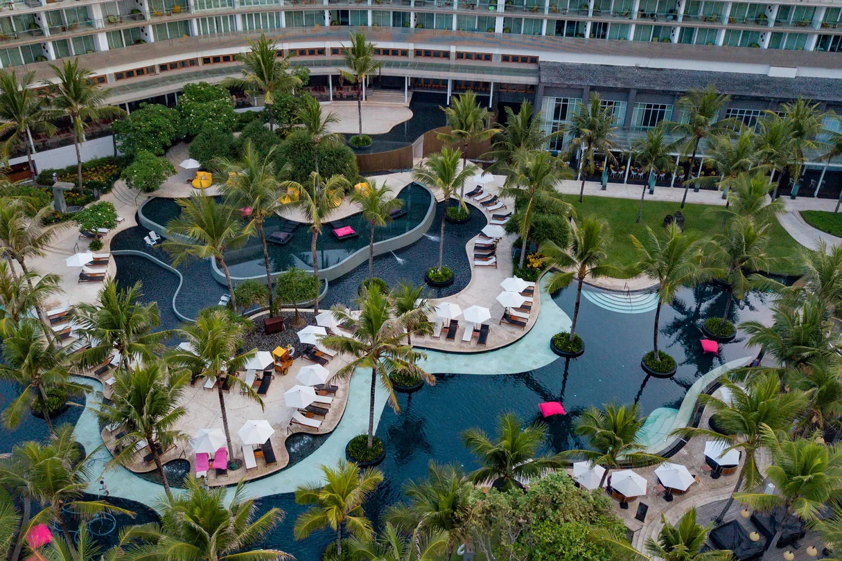Aerial of W Bali Seminyak's curving resort pool with cabanas and palms by the beach