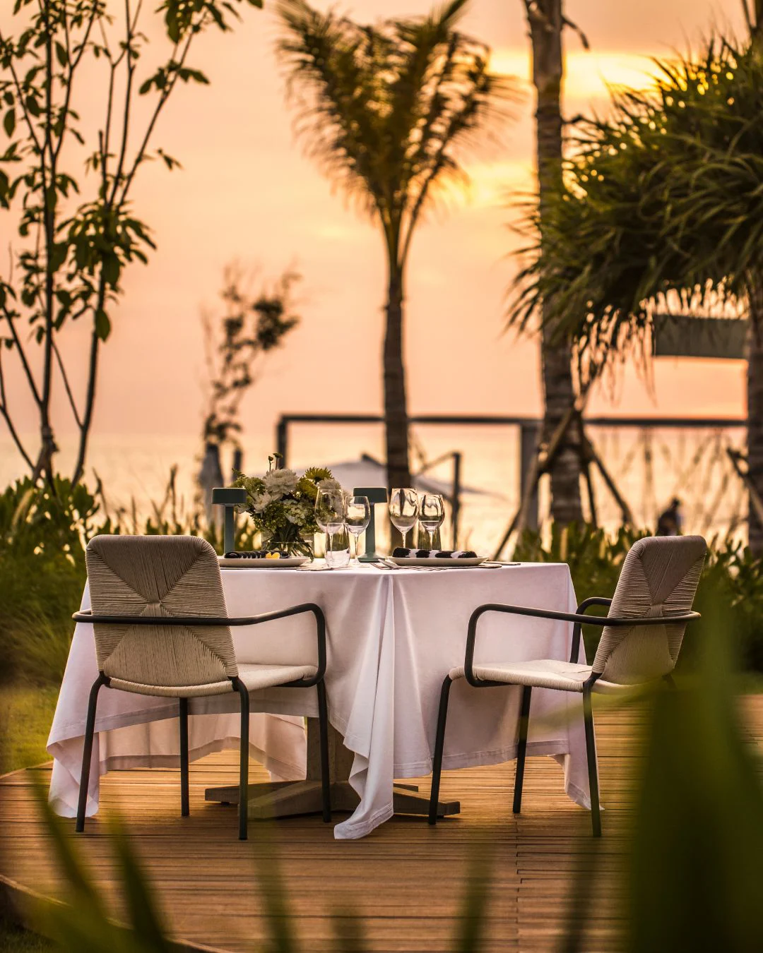Private beachfront dinner for two set on a timber deck at sunset, Canggu, Bali